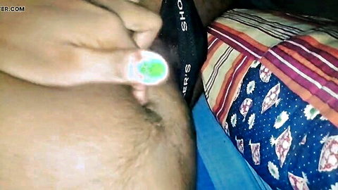 Brown-skinned man on colorful bed pulls down black shorts exposing hairy pubic mound