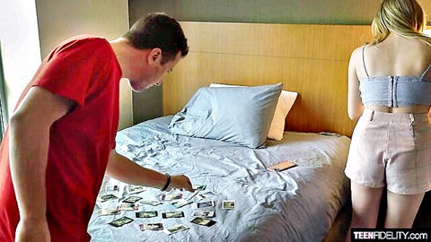 Blonde teen in tight shorts stands as guy views photos on bed