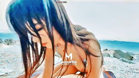 Seductive Asian teen with perky tits lies topless on rocky beach looking back passionately
