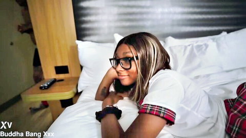 Ebony babe in glasses and plaid skirt teases seductively on bed with tattoo peek
