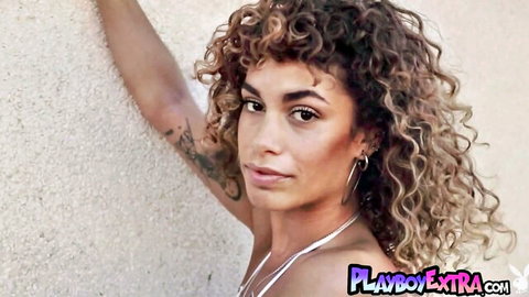 Sensual curly-haired tattooed Latina babe posing erotically outdoors in tight top