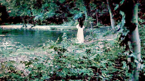 Mysterious babe in white dress standing by pond in lush green forest
