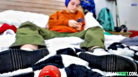 Juniper Ren as tomboy in orange hoodie and green pants, casual bedroom pose