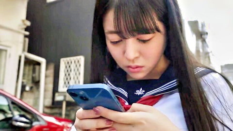 Cute Japanese schoolgirl in sailor uniform holding blue iPhone smiling outdoors