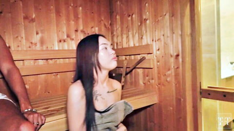 Asian woman with long dark hair and shoulder tattoo topless in sauna with man