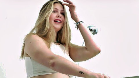 Tanned blonde bombshell with huge tits smiling and posing in tight white tank top