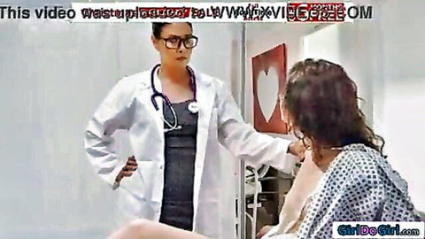 Doctor in white coat stands over topless patient exposing huge bare tits in lesbian medical exam