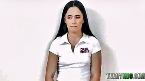 Serious-faced Latina teen in tight white collared GAP shirt against plain wall