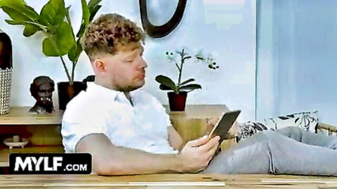 Ginger stud in open white shirt sits legs spread holding tablet in kitchen on MYLF