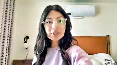 Latina ski instructor vlogging in cozy bedroom, smiling brunette with glasses