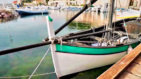 Green and white boat docked in sunny marina with clear water