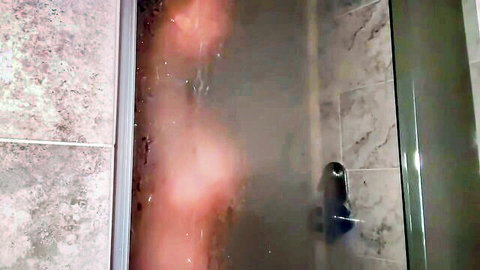 Blurry nude woman showering in steamy foggy glass enclosure, water cascading over silhouette.