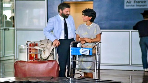 Vintage suited man chats with brunette woman in dress at Air France airport counter