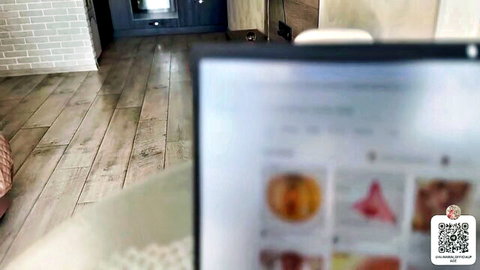 Laptop screen displays grid of suggestive porn thumbnails with nude women, peach emojis and pink pussy closeups in cozy room