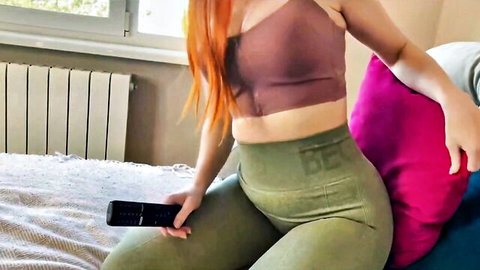 Redhead milf in tight green leggings seduces on bed holding remote