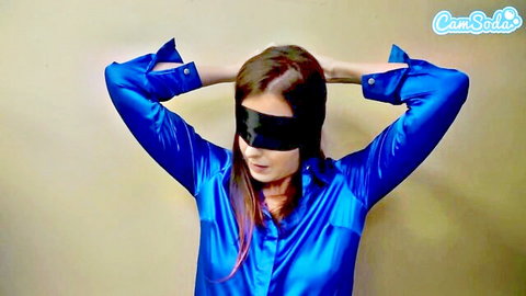 Blindfolded teen in shiny blue satin blouse, arms raised teasingly