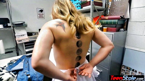 Skinny blonde teen with spine tattoos pulls down white pants exposing bare back in police office