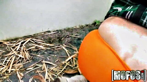 Pale woman exposing juicy white ass cheeks from tight orange thong outdoors on dirty floor near man's legs