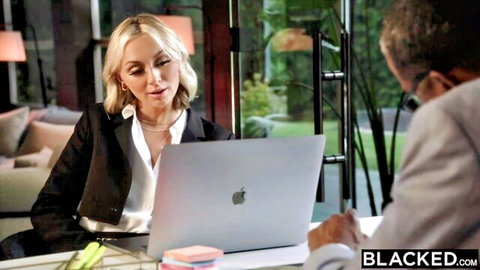 Blonde office woman in suit meets suited black man at desk with laptop