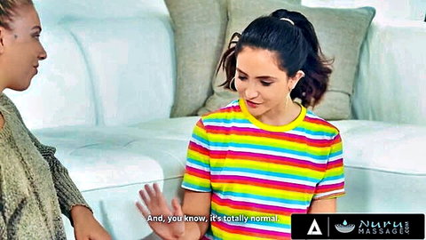 Two hot stepsisters chatting casually in colorful striped top on couch for Nuru Massage threesome