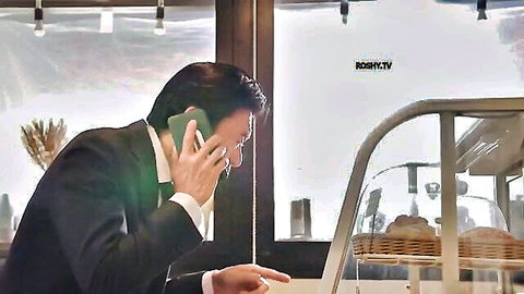 Suited man with black hair talking on green phone near bakery bread display