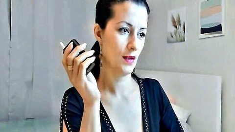 Sexy brunette MILF cougar smoking cigarette in black studded dress showing cleavage