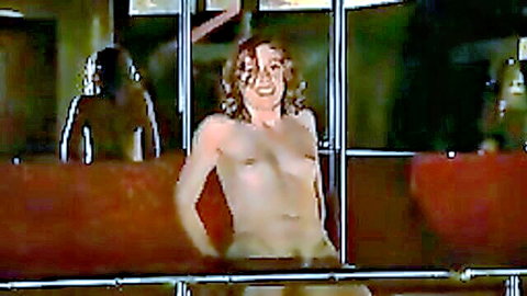 Topless curly redhead smiles exposing bare tits behind prison bars in amateur tease