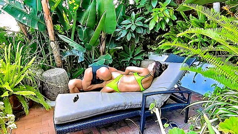 Brunette bikini babe lies face down on pool lounger as muscular black stud positions behind her outdoors