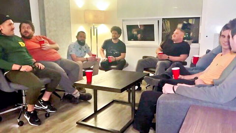 Group of bearded men sitting around table holding red solo cups in casual lounge party.