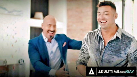 Bald gay daddy in blue suit touches smiling brunette hunk in shiny shirt in kitchen
