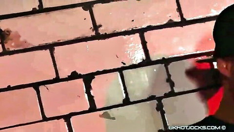 UK jock in cap pissing on pink brick wall outdoors