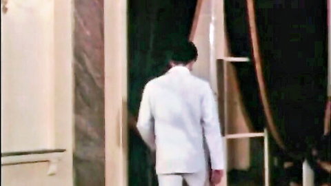 Man in white suit walks toward doorway in vintage retro erotic film scene