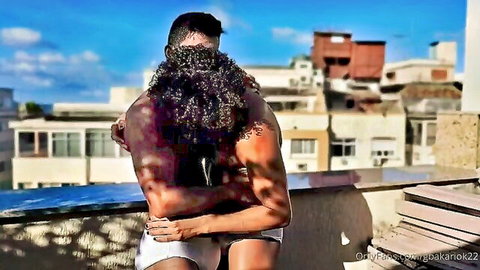 Muscular Brazilian hunk hugs partner from behind in tight shorts, urban vibe