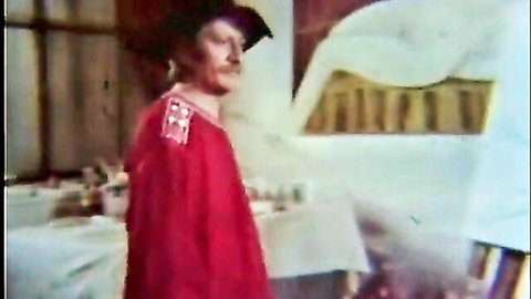 Vintage redheaded man in red cape and hat stands profile in kitchen setting