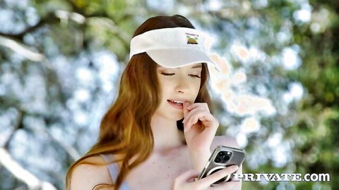 Hazel Moore redhead in white visor teases with phone outdoors