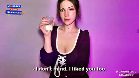Busty brunette in low-cut purple lace top holds glass of creamy liquid showing deep cleavage