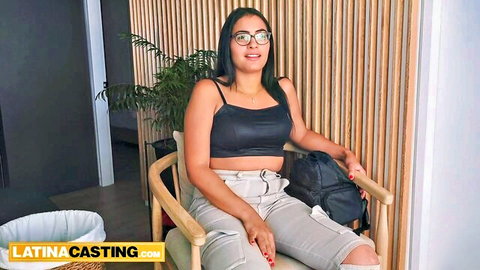 Colombian Latina in glasses and black top, smiling in casual casting pose