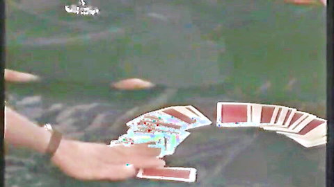 Man's hand dealing red-backed playing cards on green poker table in pixelated VHS footage