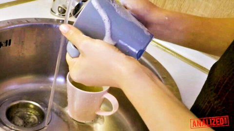 Hands washing soapy blue mug in kitchen sink with pink mug below