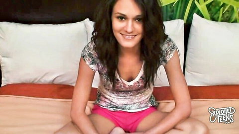 Brunette teen babe smiles spreading legs in tight pink shorts and tank top on bed