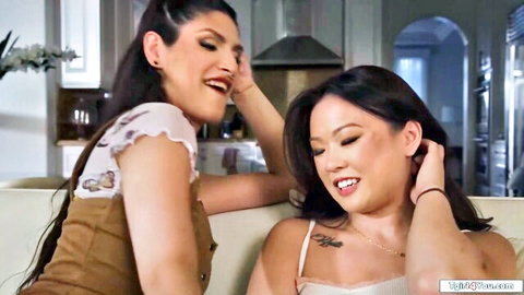 Two sexy smiling brunettes playfully touching hair on couch in kitchen