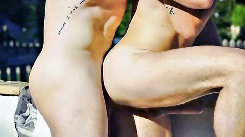 Two muscular nude young men outdoors, one bent over exposing bare ass as the other grabs his hips dominantly.