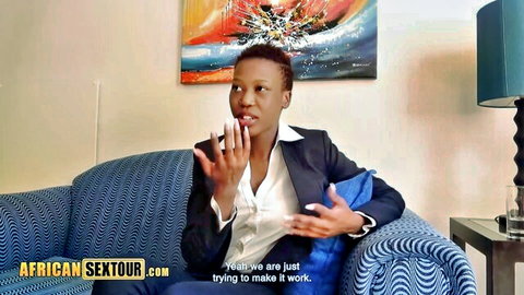 African babe in suit gesturing on couch, big natural tits hinted