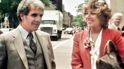 Vintage couple in suits smiling and chatting on urban street with cars and truck in background