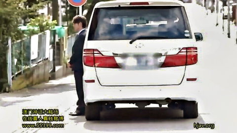 Suited man stands behind white SUV on Japanese street with hjw.org watermark