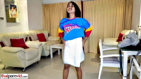 Cute petite Thai teen in short white skirt and colorful please t-shirt teasing in living room
