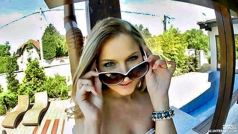 Smiling blonde babe with small tits and deep cleavage teases poolside holding sunglasses