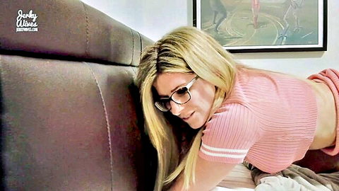 Blonde MILF with glasses in pink crop top teases underboob pressing against bed headboard