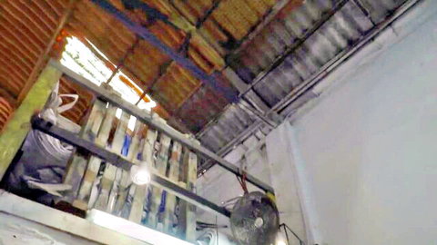Blurry indoor view of wooden beams, corrugated roof, railing, hanging fabric and ceiling fan with no people visible