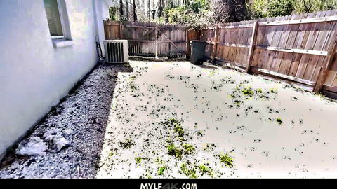 Empty backyard patio with white wall, wooden fence, AC unit, trash bin and gravel ground